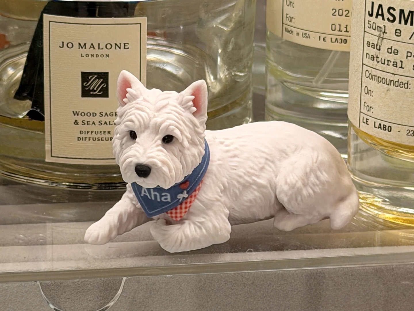 Real photograph of the finished Aha dog figurine displayed in front of glass fragrance bottles